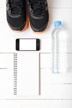 fitness equipment : running shoes,drinking water,notebook and phone on white wood table