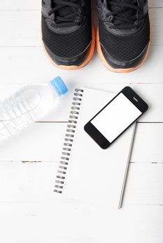 fitness equipment : running shoes,drinking water,notebook and phone on white wood table