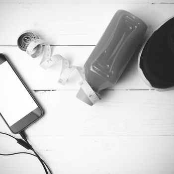 running shoes,orange juice,measuring tape and phone on white wood background black and white tone color style