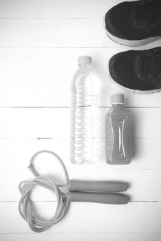 fitness equipment : running shoes,jumping rope,drinking water and orange juice on white wood background black and white tone color style