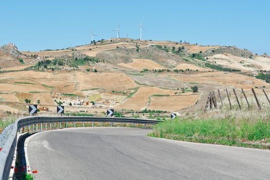 Winding Asphalt Road on the Background of the Modern Wind Turbines in Sicily