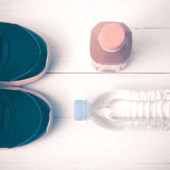 running shoes,drinking water and orange juice on white wood table vintage tone color style