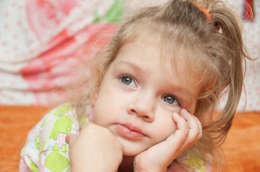 Cheerful three year old girl lying on the bed and looked to the left 