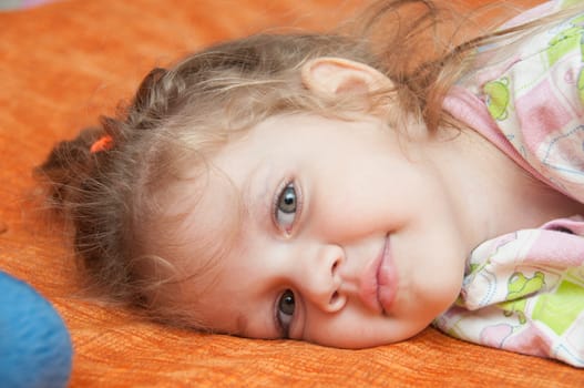 Cheerful three year old girl lying on the bed and looked into the frame 