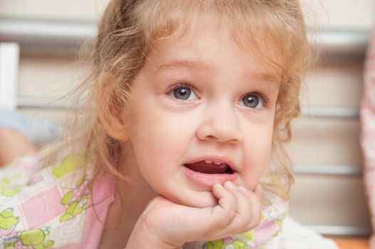 Cheerful three year old girl lying on the bed and looked past the frame 
