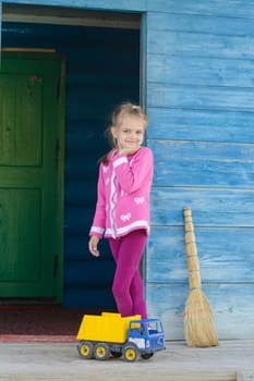 Six year old girl playing with toy dump truck on the porch of a wooden house