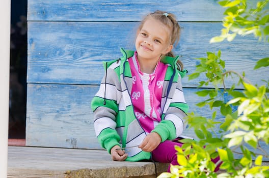 Six year old girl sitting on the porch of a wooden house and smiling happily
