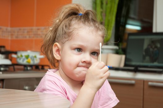 The three-year girl with a funny looking angrily at the cotton swab while sitting at the kitchen table