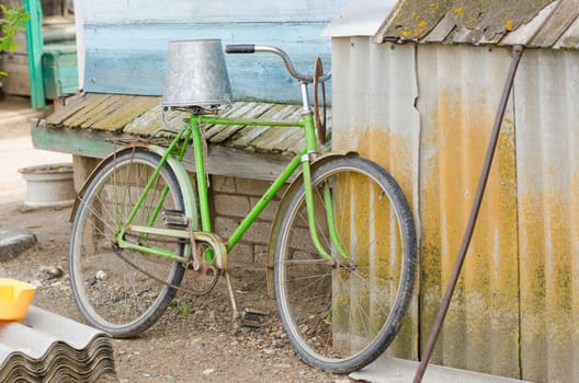 old bicycle with a bucket upside down on the saddle is at the wooden house
