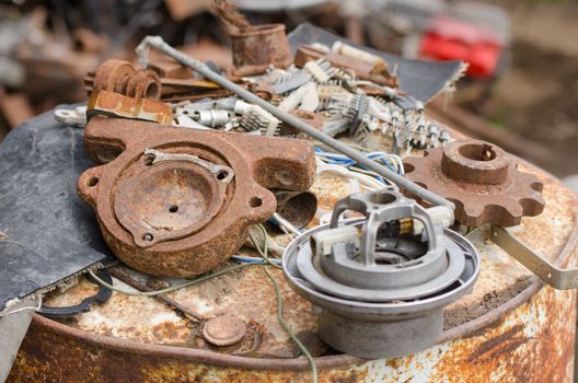 A pile of old broken machinery, spare parts and rusty pieces of iron lying on a rusty barrel