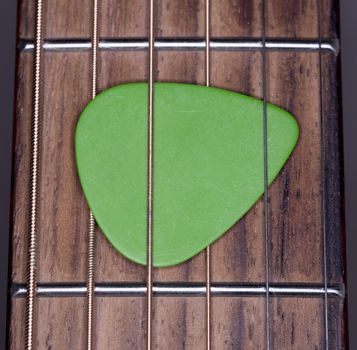 Green Plectrum Stuck in Steel Strings close up macro image.