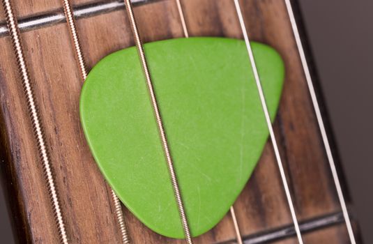 Green Plectrum Stuck in Steel Strings close up macro image.