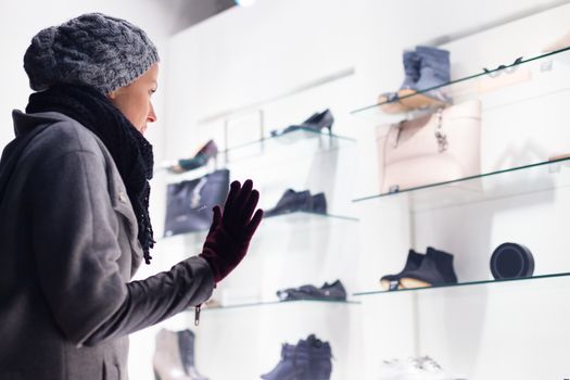 Casualy winter dressed lady window shopping in front of sinfully expensive boutique store dispaly window. Customer woman in shopping street, looking at window, outdoor.