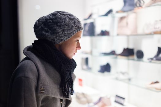 Casualy winter dressed lady window shopping in front of sinfully expensive boutique store dispaly window. Customer woman in shopping street, looking at window, outdoor.