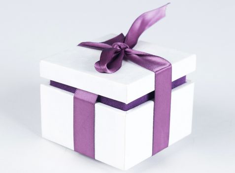 White gift box with violet ribbon bow, isolated on white background