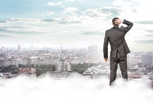 Businessman standing on clouds looking at city, rear view