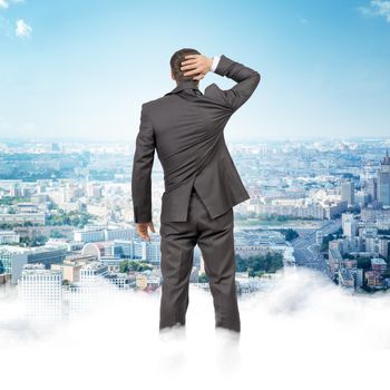 Businessman standing on clouds looking at city, rear view