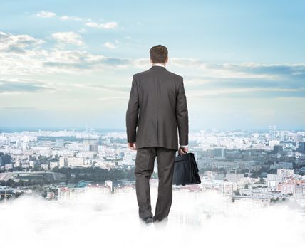 Businessman standing on clouds looking at city, rear view