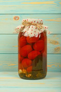 One big glass jar of homemade pickled tomatoes with dotted textile top decoration at blue painted vintage wooden surface