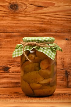 One big glass jar of homemade pear compote with green checkered textile top decoration at brown vintage wooden surface