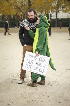 FRANCE, Paris : A woman disguised as a dinosaur holds a sign reading Dinos did not know but we do on the Champ-de-Mars, near Paris Eiffel tower on December 12, 2015 as thousands of people demonstrate for environment protection.  