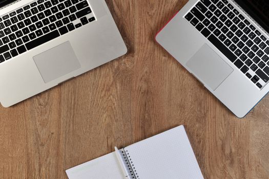 person writing in notebook infront of two laptops