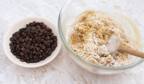 Chocolate chips in a bowl ready to be added to raw cookie dough with a wooden spoon