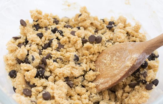 Stirring chocolate chips into raw cookie dough with a wooden spoon