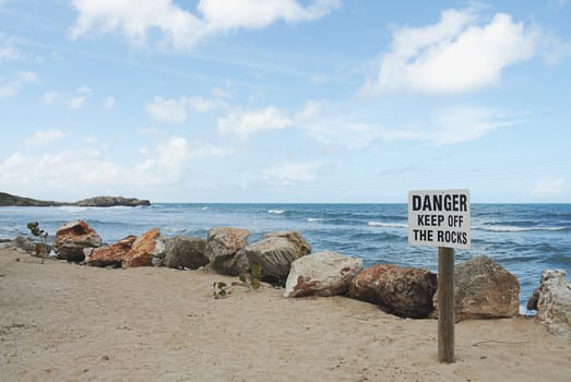 sign on beach with Danger keep off the rocks