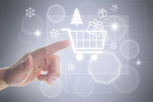 Finger selecting a shopping cart symbol on a touch screen surrounded by christmas icons 