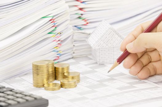 Man is auditing account with pencil and step pile of gold coins on the statement finance account have blur calculator and house with pile of document as foreground and background.