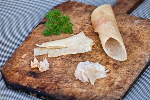 Pig skin slices, garlic and persil on wooden plate