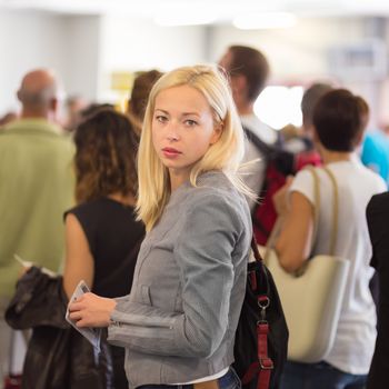 Young blond caucsian woman waiting in line with plain ticket in her hands. Lady standing in a long queue to board a plane.