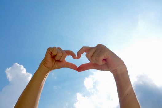 Hands shape of heart beneath blue sky