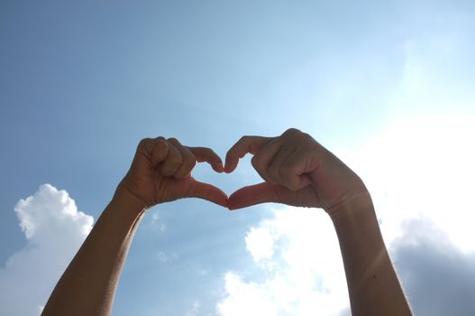 Hands shape of heart beneath blue sky