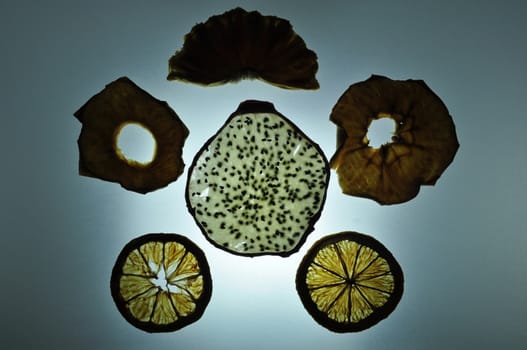 Mixed dried sliced fruit (pitaya - dragonfruit, apple, pineapple, orange - citrus) in silhouette on lighting desk 