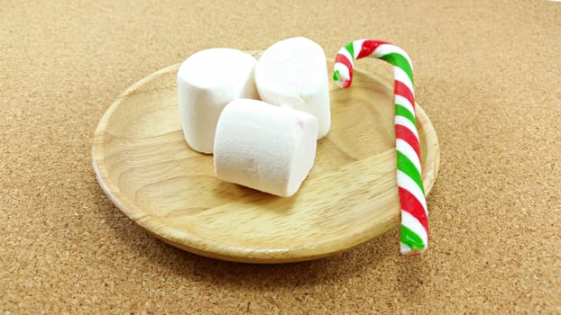 Christmas marshmallow and candy cane on the wooden plate