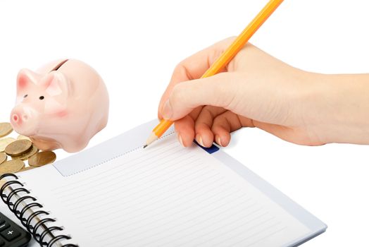Females hand writing within pen in notebook and piggy bank on isolated white background