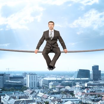 Businessman sitting on rope above city and looking at camera