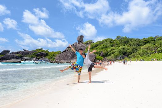 Tourist couple raised his arms and legs with happy on beach near the sea under blue sky and cloud of summer at Koh Similan Island in Mu Ko Similan National Park, Phang Nga province, Thailand