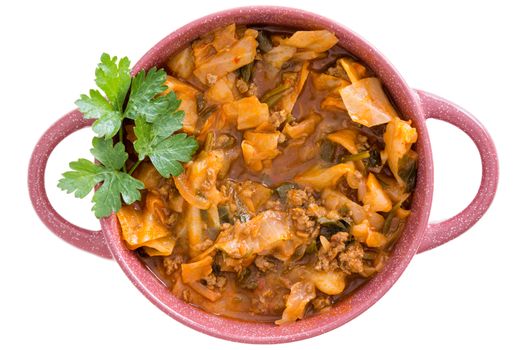 Nutritional cabbage soup with ground beef mince and seasoning garnished with fresh parsley served in a pink bowl for an appetizing winter meal, overhead on white