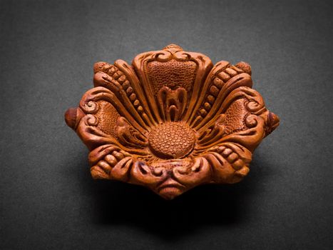 Front view of a beautifully carved designer handmade clay lamp on dark background.