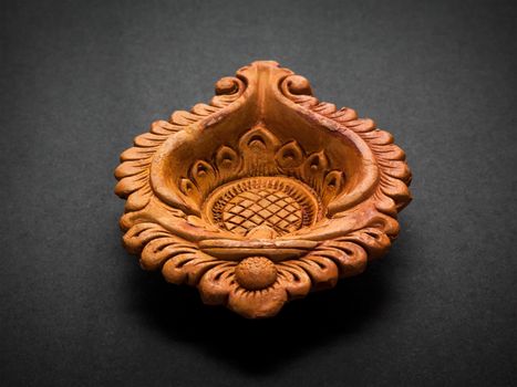 Front view of a beautifully carved designer handmade clay lamp on dark background.