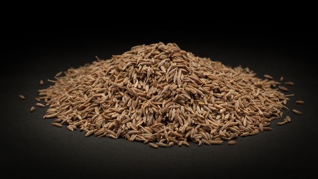 Pile of Organic Cumin seed (Cuminum cyminum) on dark background.