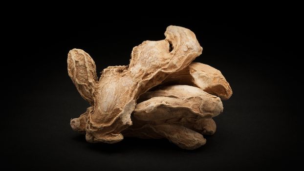 Pile of Organic Dried Ginger root or Sonth (Zingiber officinale) on dark background.