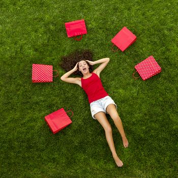 Beautiful and happy young woman lying on the grass surrounded by red gift bags