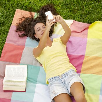 Smiling young woman lying on a blanket and making a selfie
