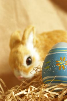 A cute Easter bunny is blurred in the background with the focus on the egg sitting in the paper shred.