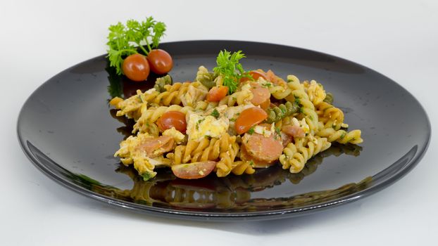 Macaroni pasta with tomato sauce and sausage on a black and white plate isolated