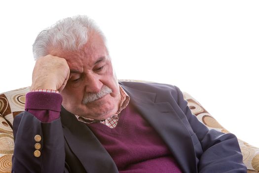 Tired elderly retired gentleman sitting thinking in a comfortable armchair resting his head on his hand with his eyes downcast, close up isolated on white